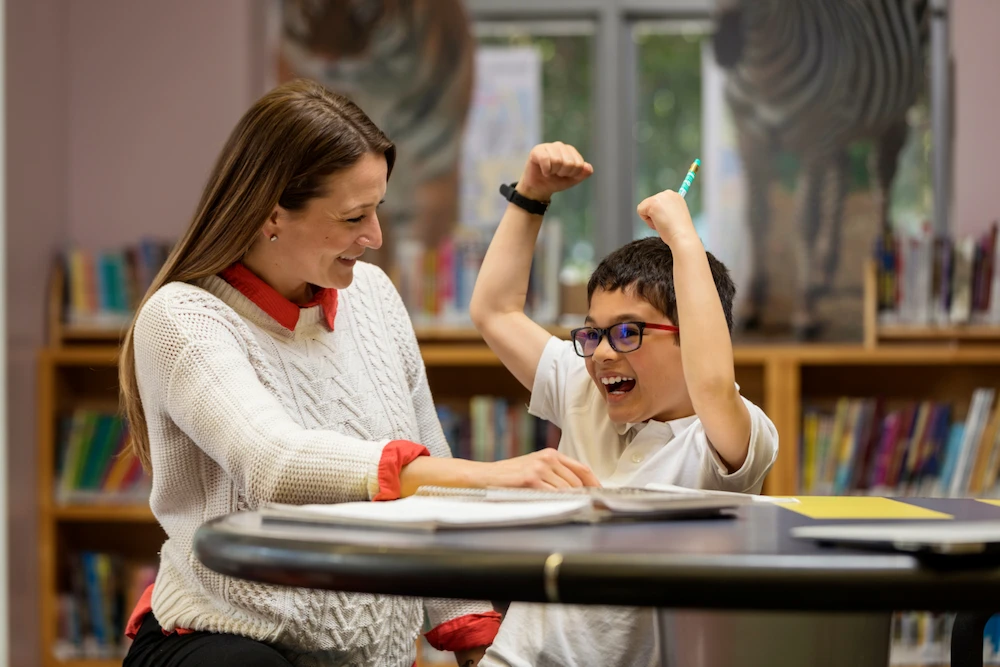 Student celebrating with arms raised while tutor smiles